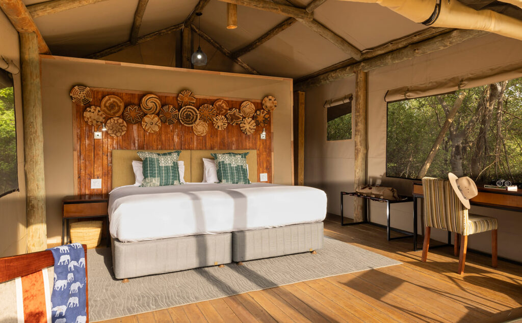 Spacious tent interior at Camp Khwai with king bed, wooden accents, and views into the surrounding bush.