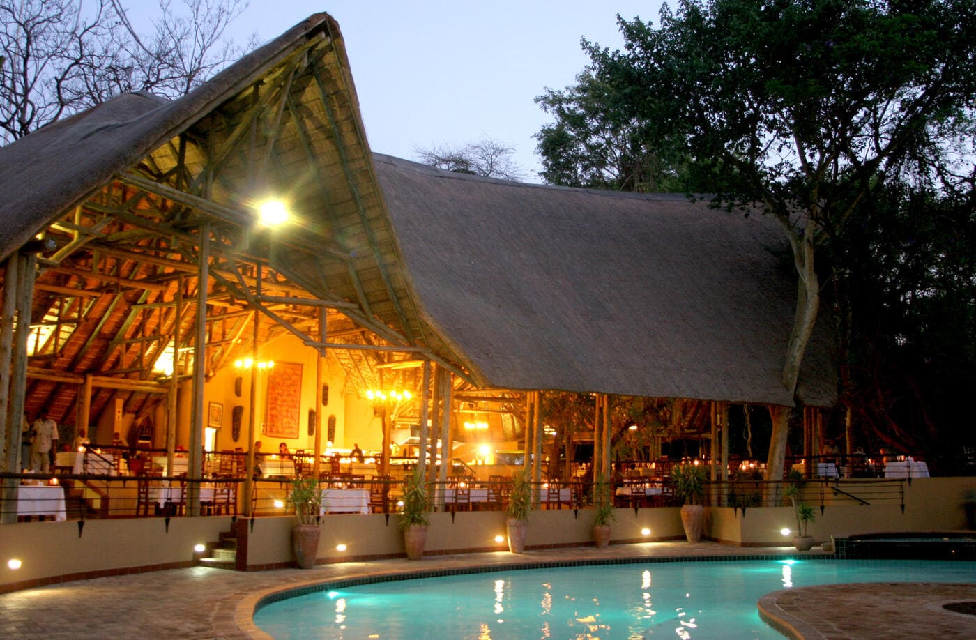 Pool and open-air lounge area at Chobe Safari Lodge, Botswana, with a thatched roof and warm evening lighting.