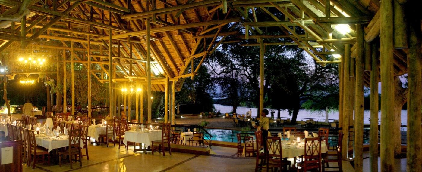 Open-air dining area at Chobe Safari Lodge overlooking the Chobe River, featuring wooden beams and candlelit tables.