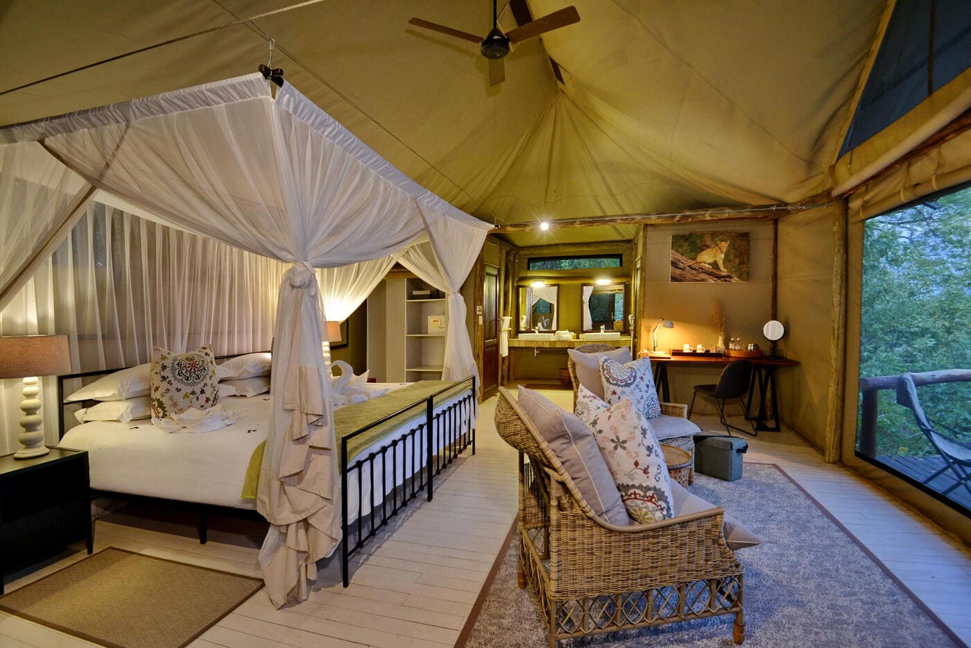 Spacious luxury tented suite at Ghoha Hills Savuti Lodge featuring a canopy bed, lounge seating, and views over the treetops.