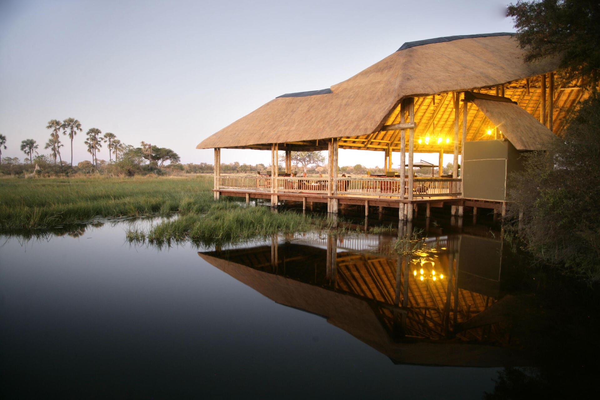 Eco-friendly Moremi Crossing Camp in Botswana’s Okavango Delta, overlooking the lagoon and surrounded by palm trees.