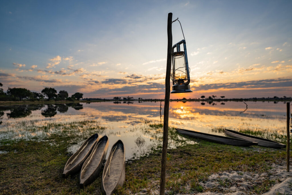Sunrise over the Okavango Delta with mokoros and lantern at the water’s edge at Pom Pom Camp.