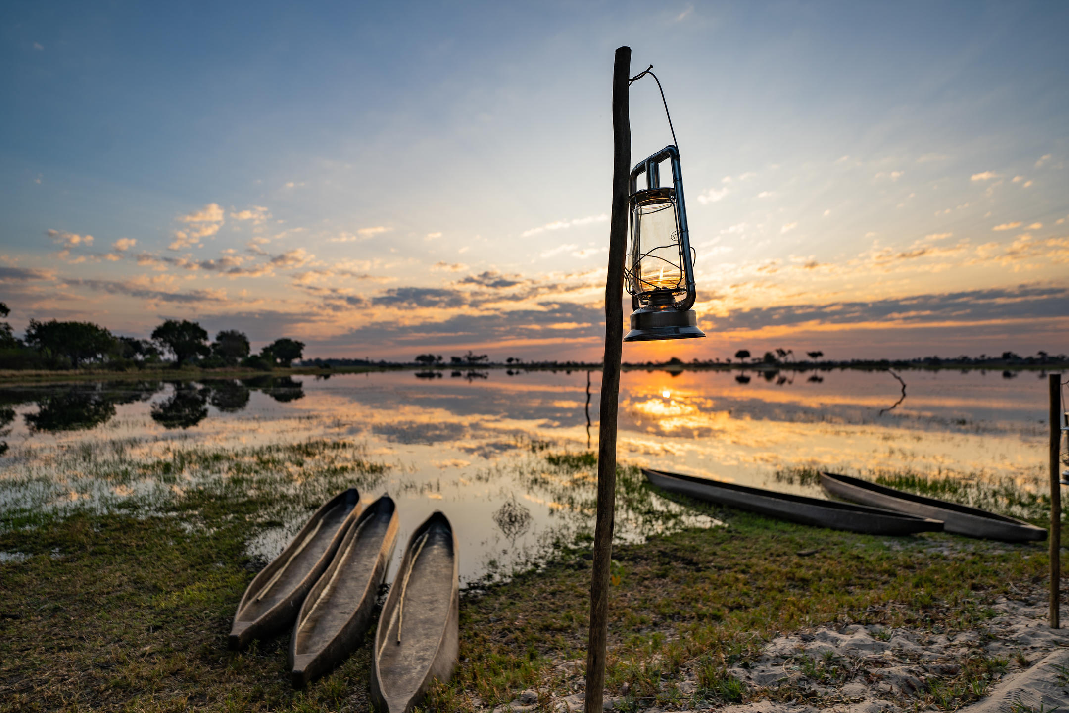 Sunrise over the Okavango Delta with mokoros and lantern at the water’s edge at Pom Pom Camp.