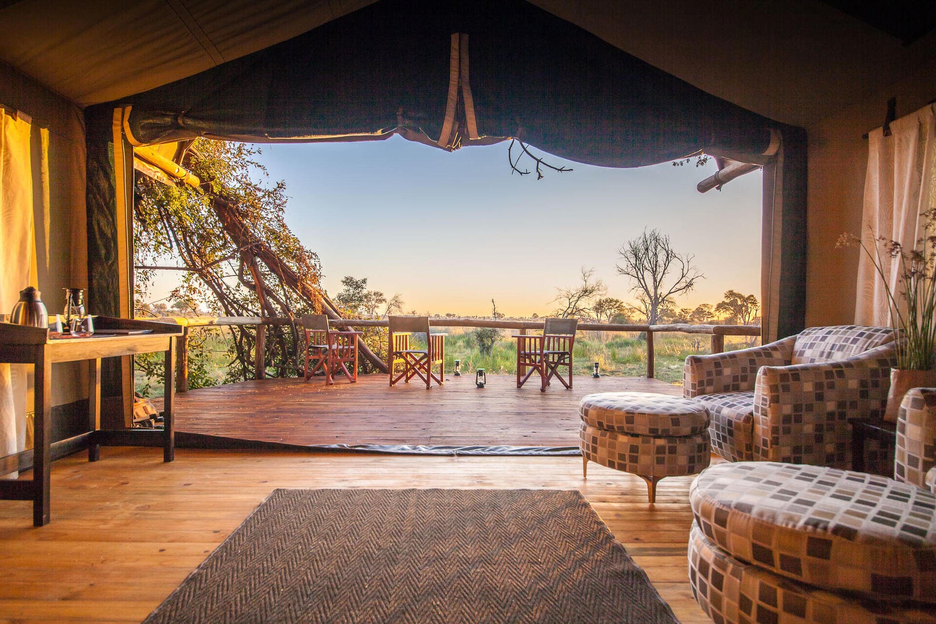 Private viewing deck of a Rra Dinare tented suite at sunset, with views across the Okavango Delta floodplains.