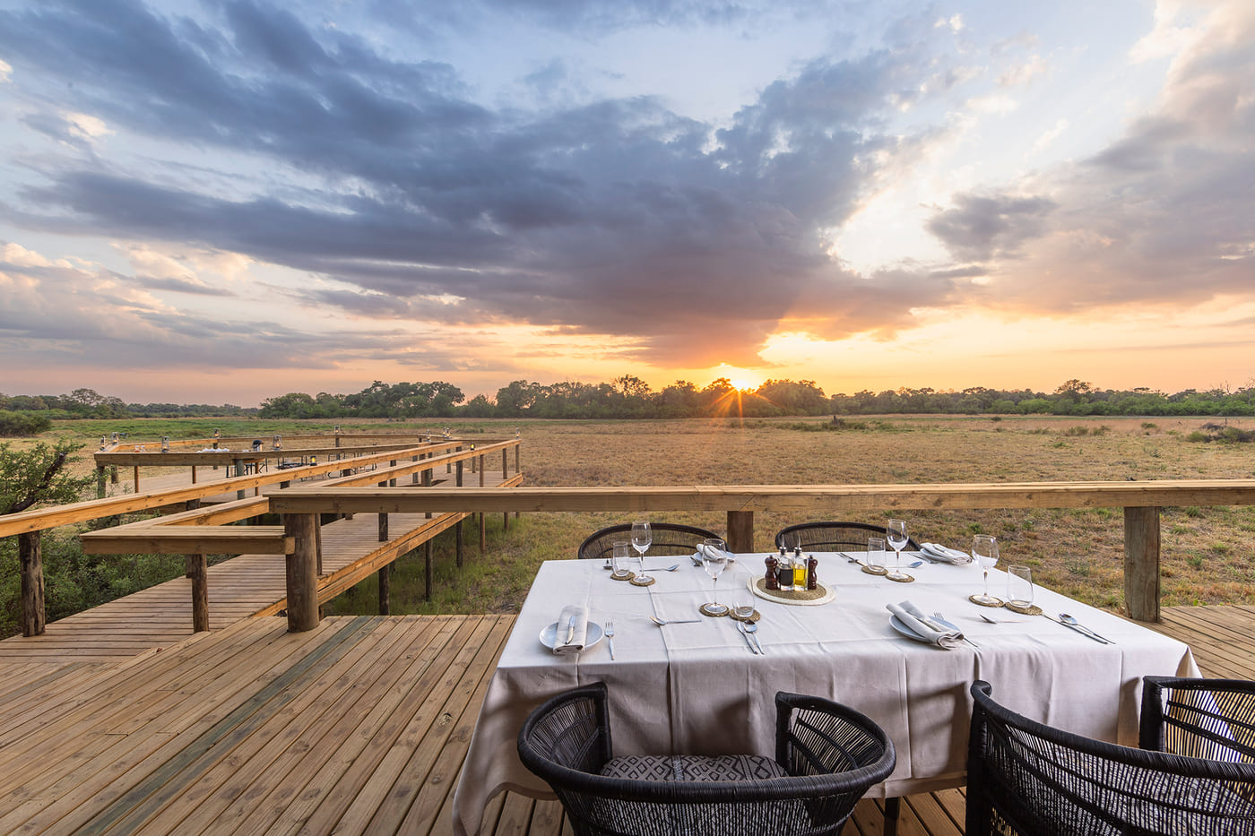 Elevated dining deck at Camp Khwai overlooking the floodplains at sunset, with panoramic views and lantern-lit tables.