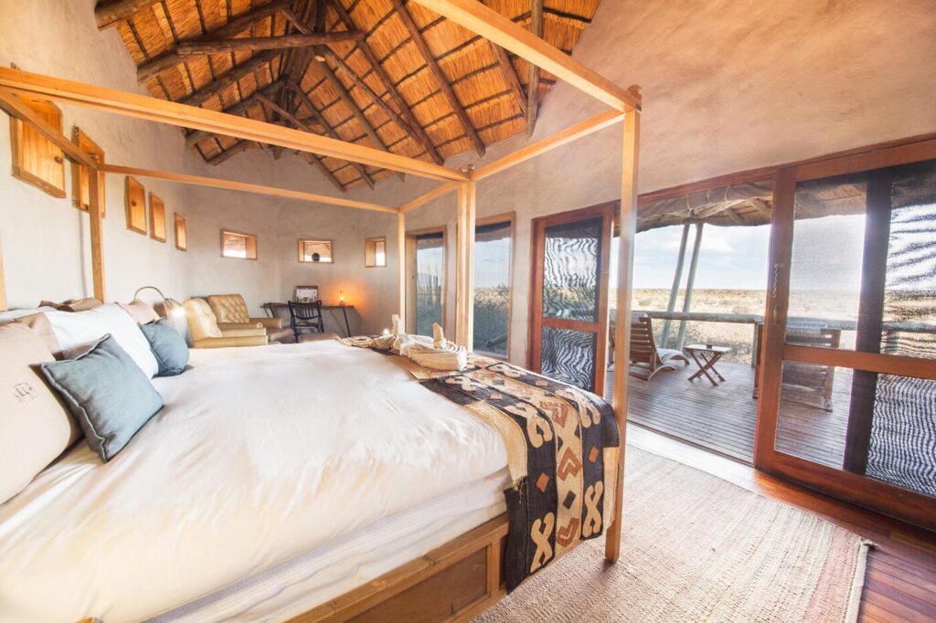 Luxury suite at Tau Pan Camp with large bed, cosy seating, and sliding doors opening onto a private deck with panoramic views of the Central Kalahari.