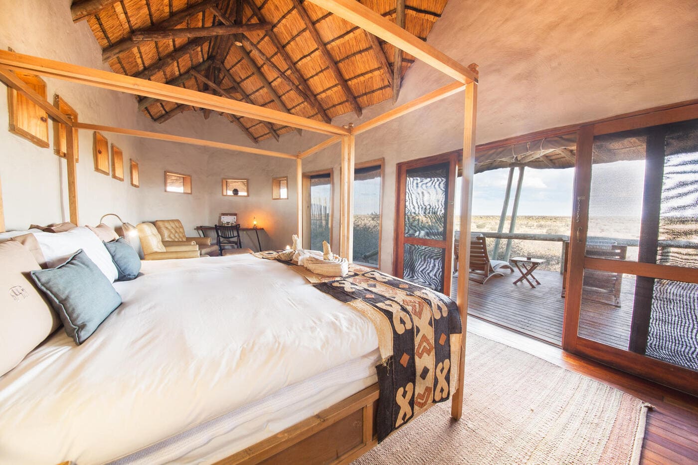 Luxury suite at Tau Pan Camp with large bed, cosy seating, and sliding doors opening onto a private deck with panoramic views of the Central Kalahari.