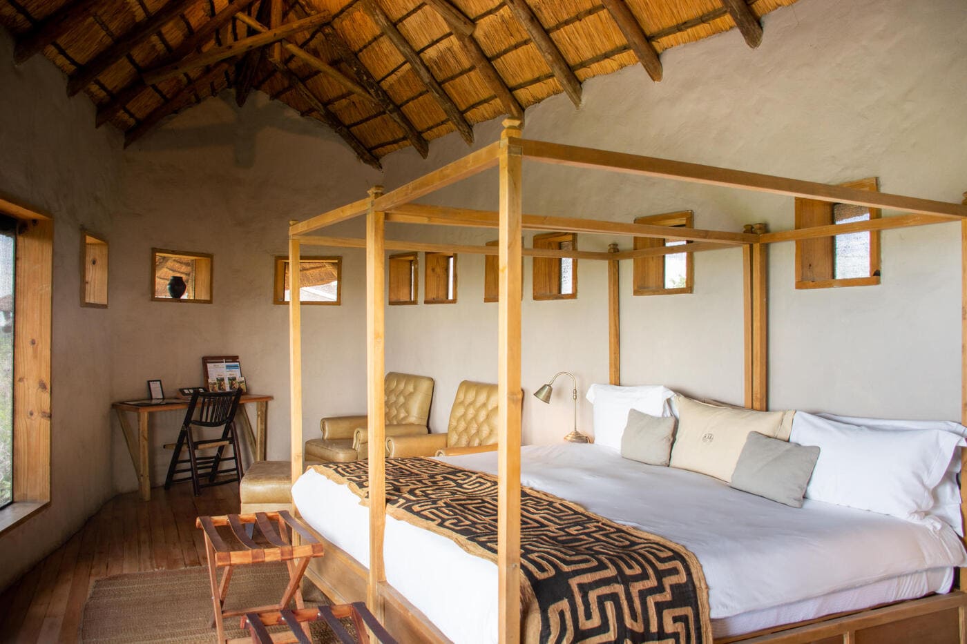 Spacious tented suite at Tau Pan Camp featuring a four-poster bed, seating area, writing desk, and natural thatch roof overlooking the Central Kalahari landscape.
