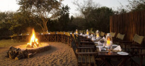 Traditional bush boma dinner at Shishangeni Main Lodge in Kruger National Park, with outdoor dining set around a campfire under the trees.