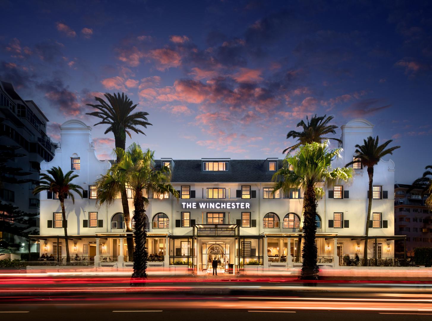 Exterior view of The Winchester Hotel on the Sea Point Promenade in Cape Town, featuring classic Cape Dutch architecture at sunset.