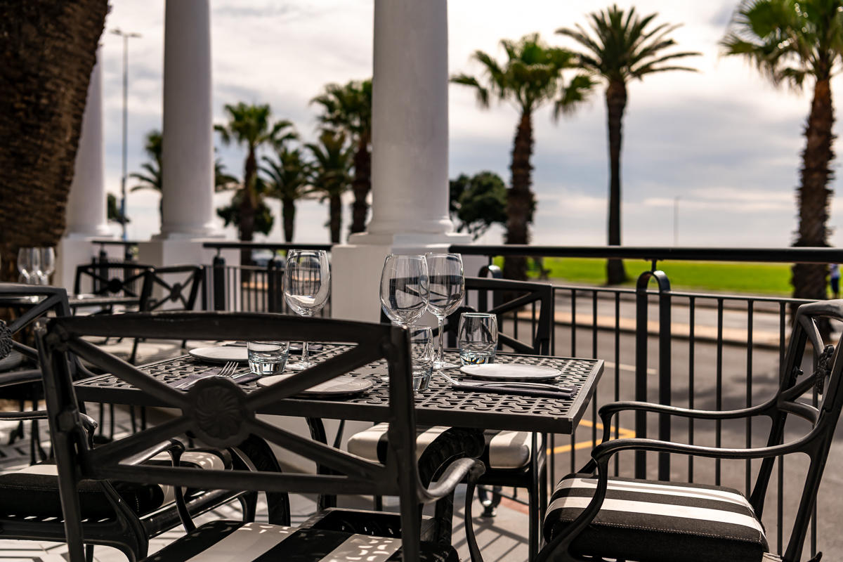 Outdoor terrace dining at The Winchester Hotel overlooking the Sea Point Promenade and Atlantic Ocean in Cape Town.